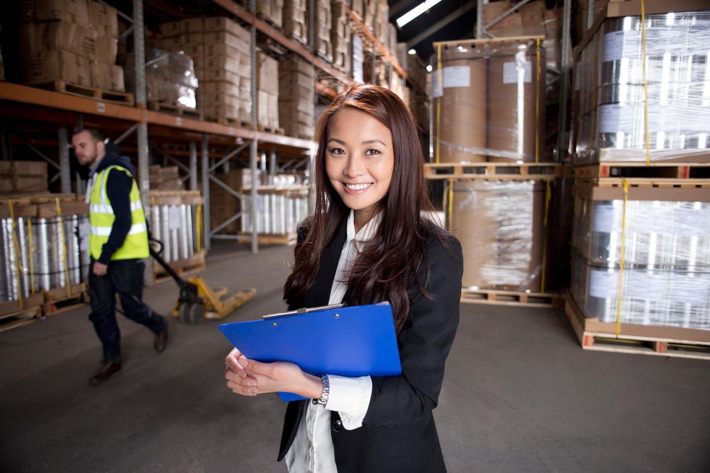A manager takes stock of the warehouse with a blue clipboard.