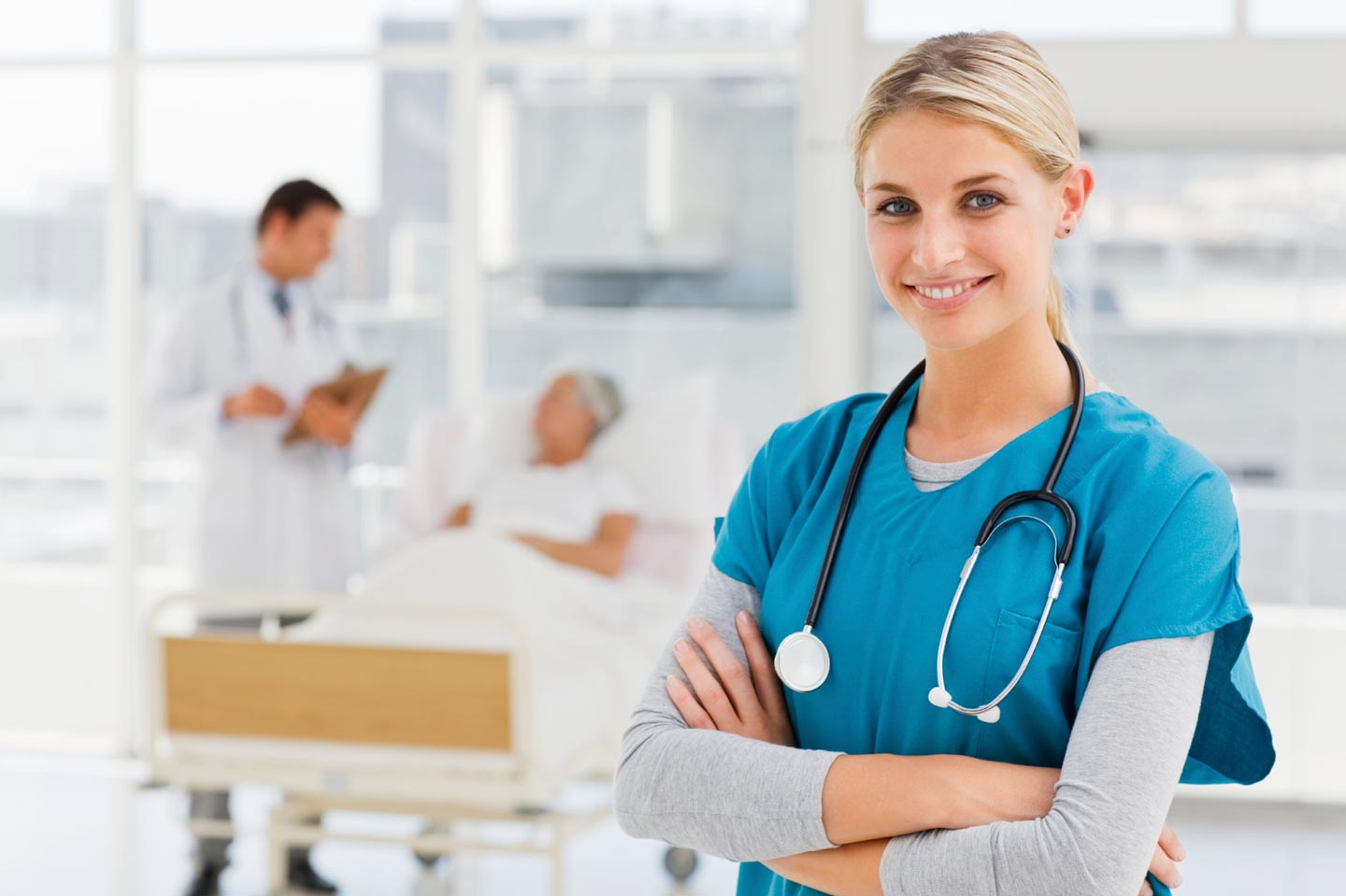 A nurse smiles as a doctor cares for a patient in a clean hospital room.